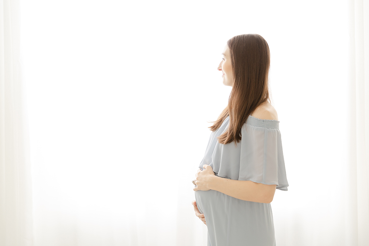 Pregnant woman in a blue dress smiles out the window