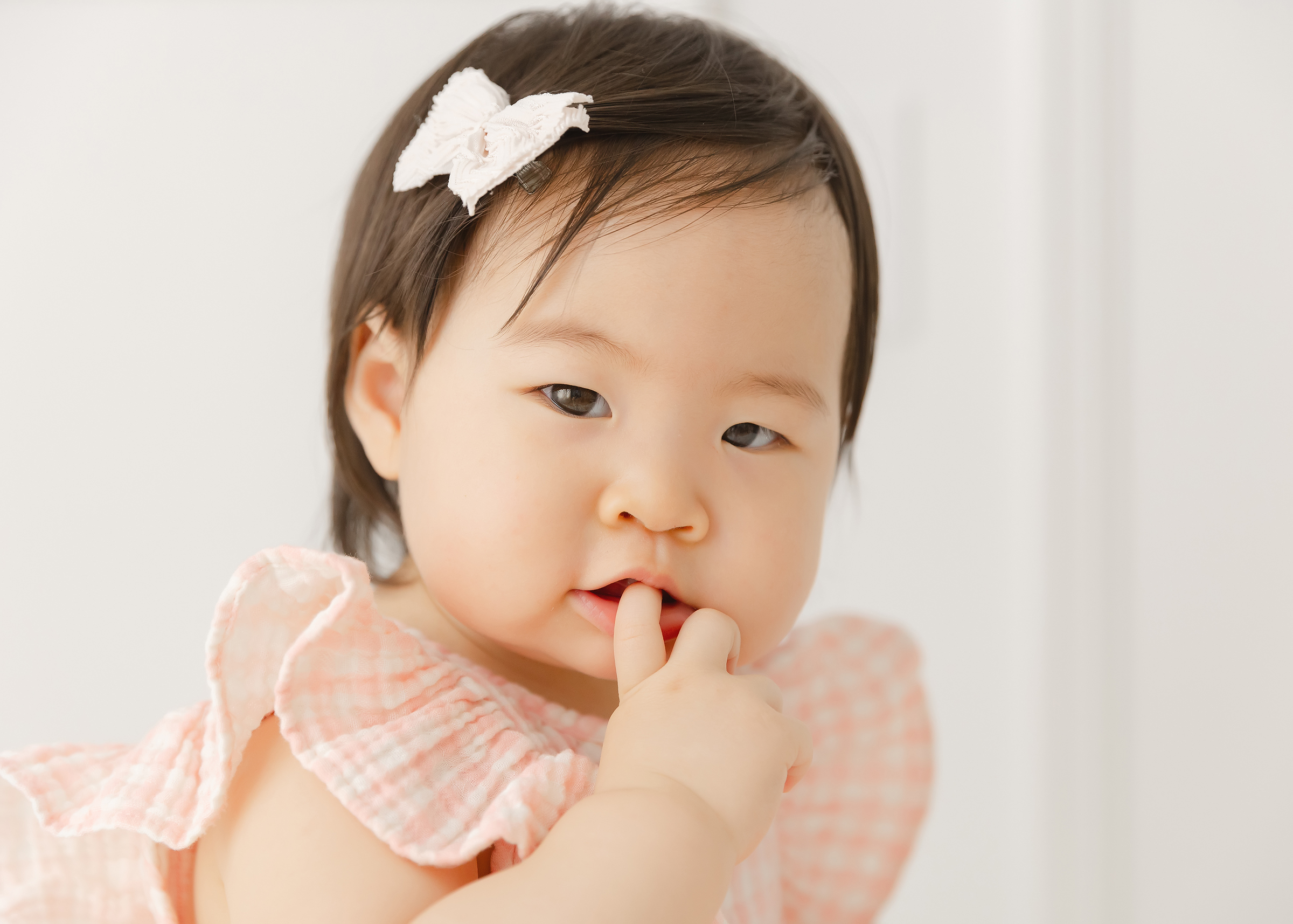 Asian baby wearing pink and looking shyly at the camera