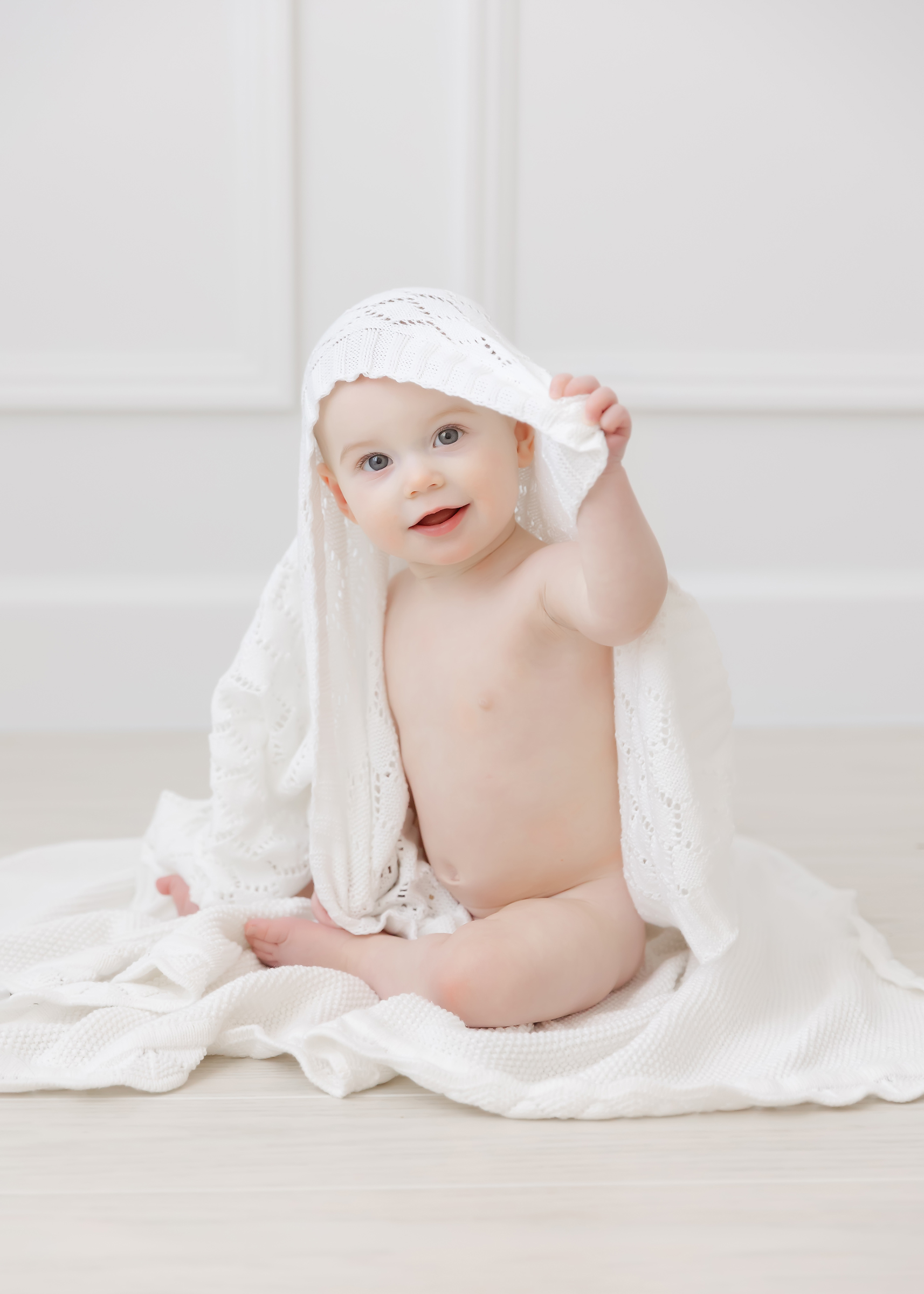 Baby smiles and pulls a white blanket off of her head