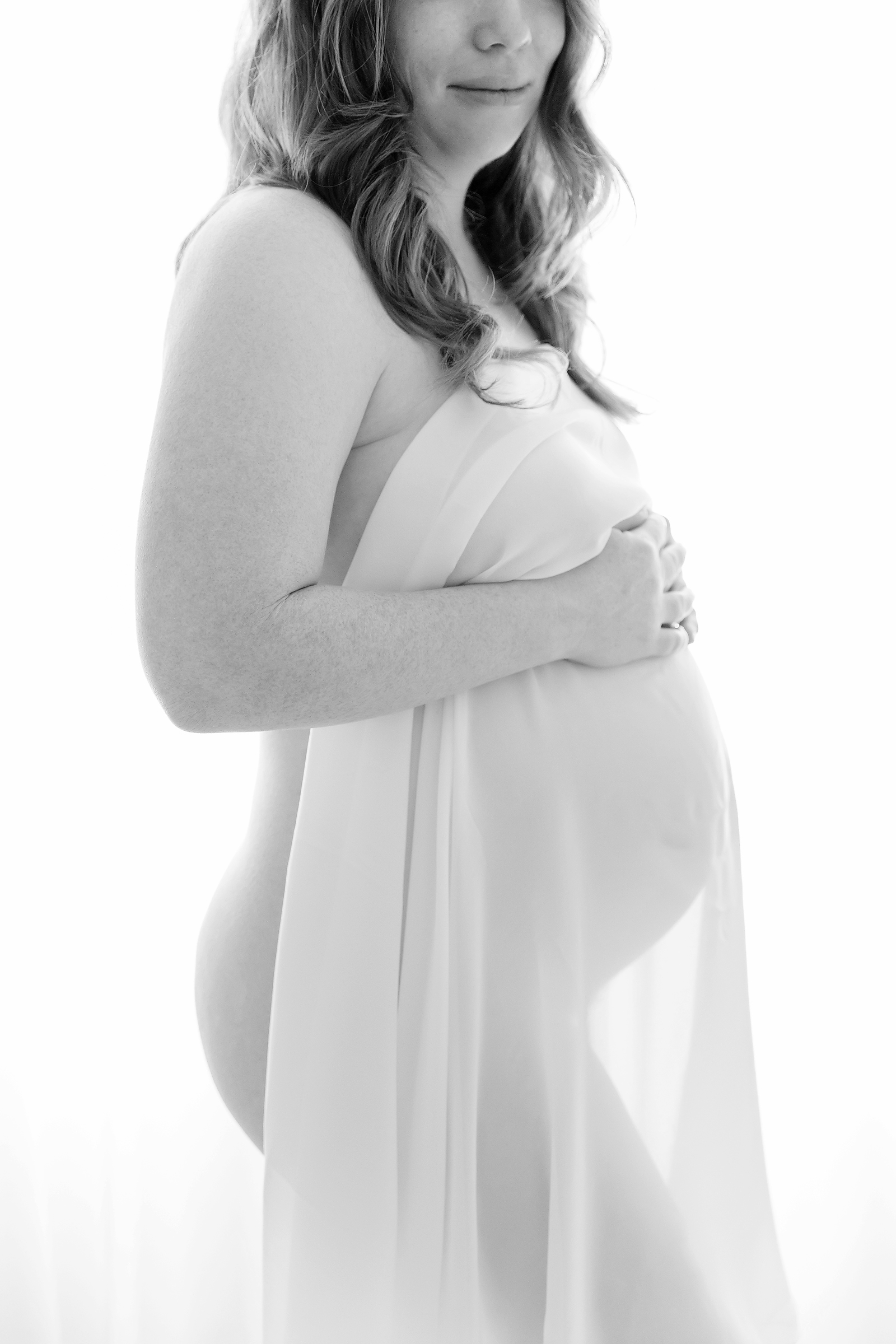 Pregnant woman silhouetted against white backdrop with a sheer drape