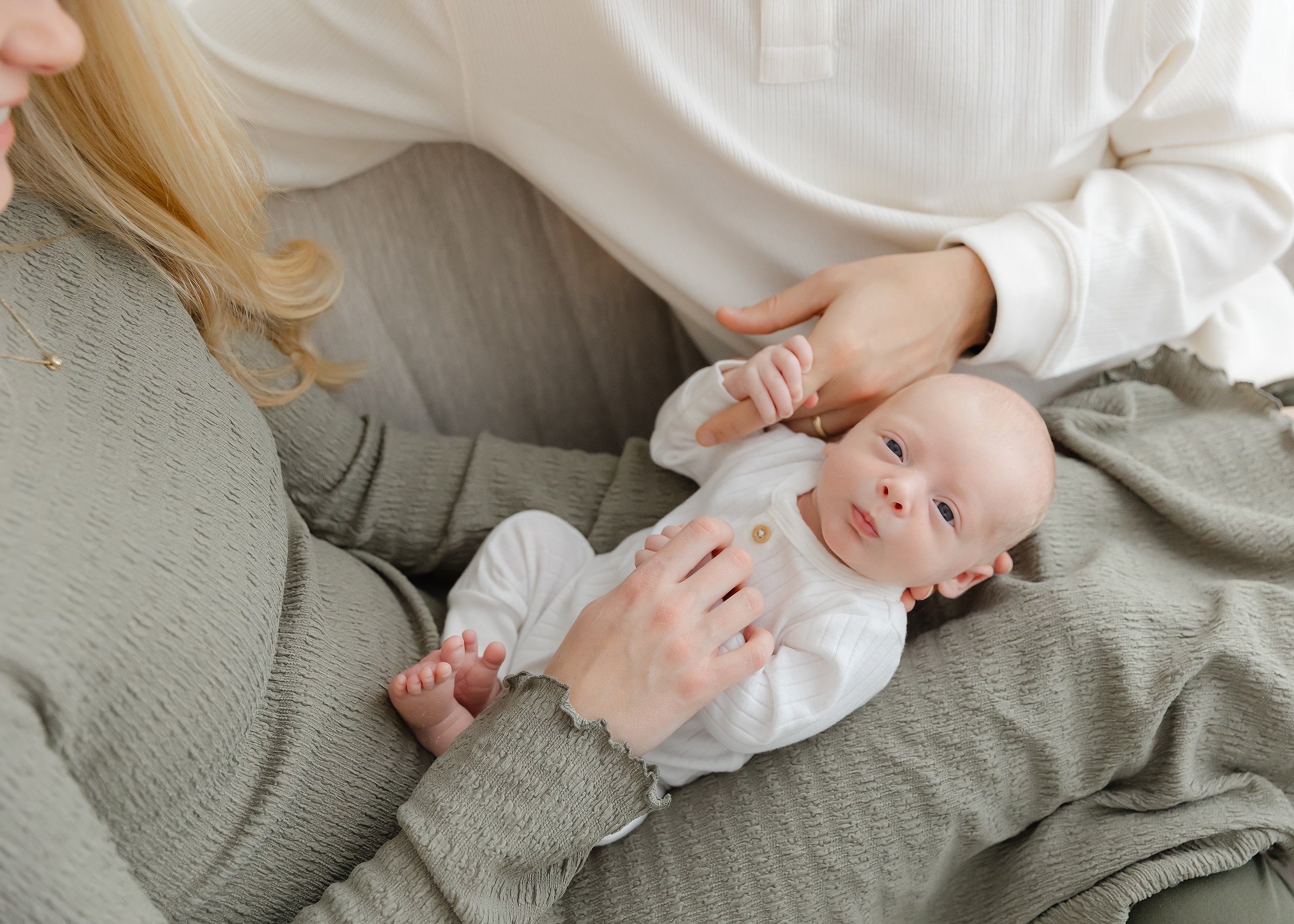 Newborn baby boy lays across the laps of his parents