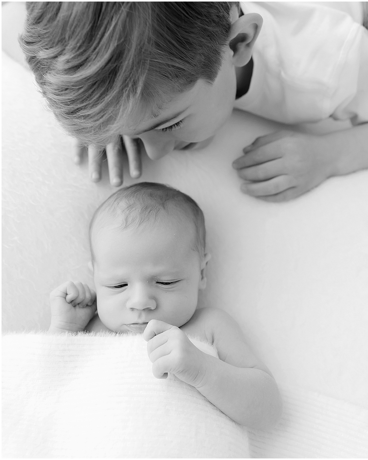 big brother smiles down at his sleeping newborn brother