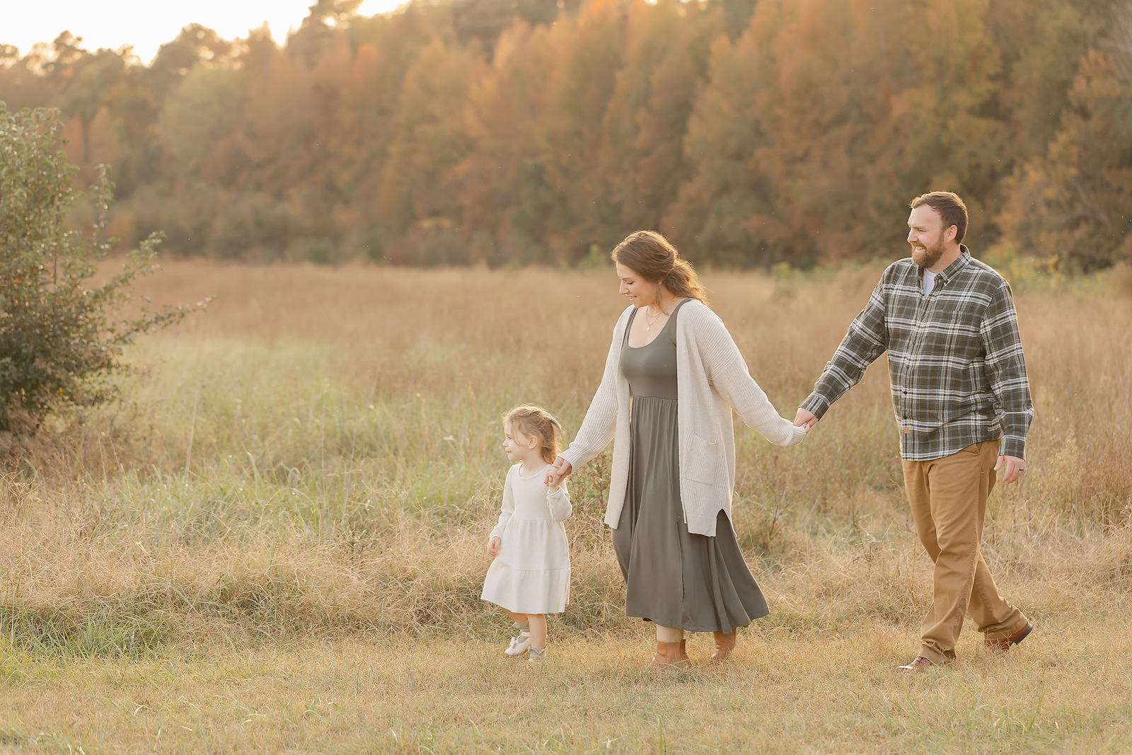 a family of three walks in golden hour during fall family mini session in raleigh nc