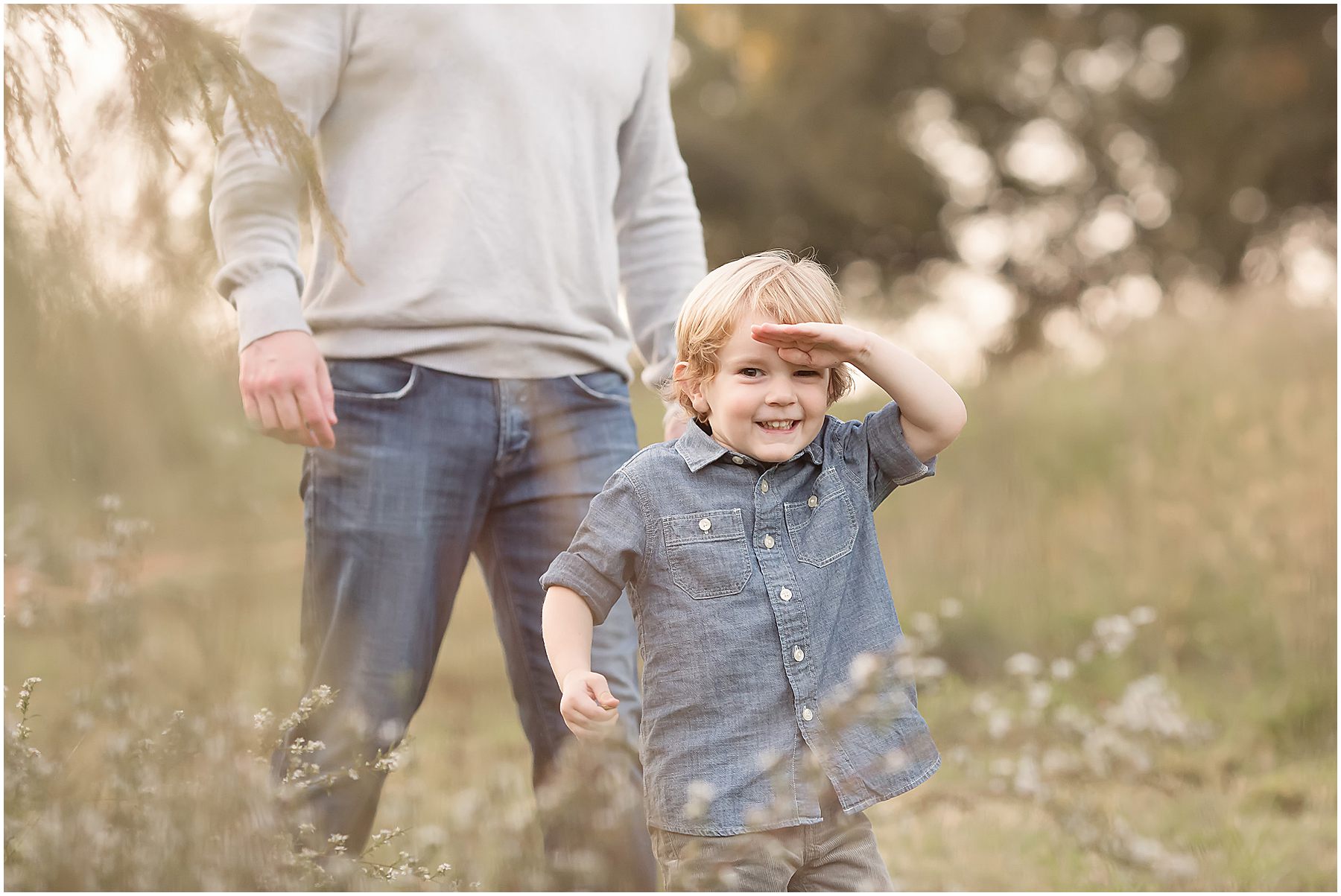 Four year old boy in a denim shirt plays in a field during a family photo session with Christy Johnson Photography