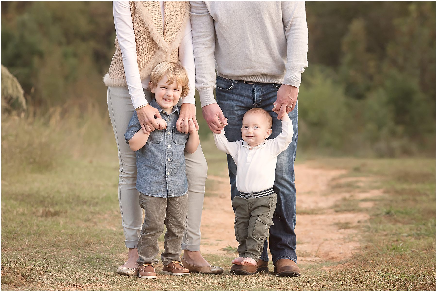 Parents stand on a path holding the hands of their little boys during a family photo session in Wake Forest, NC