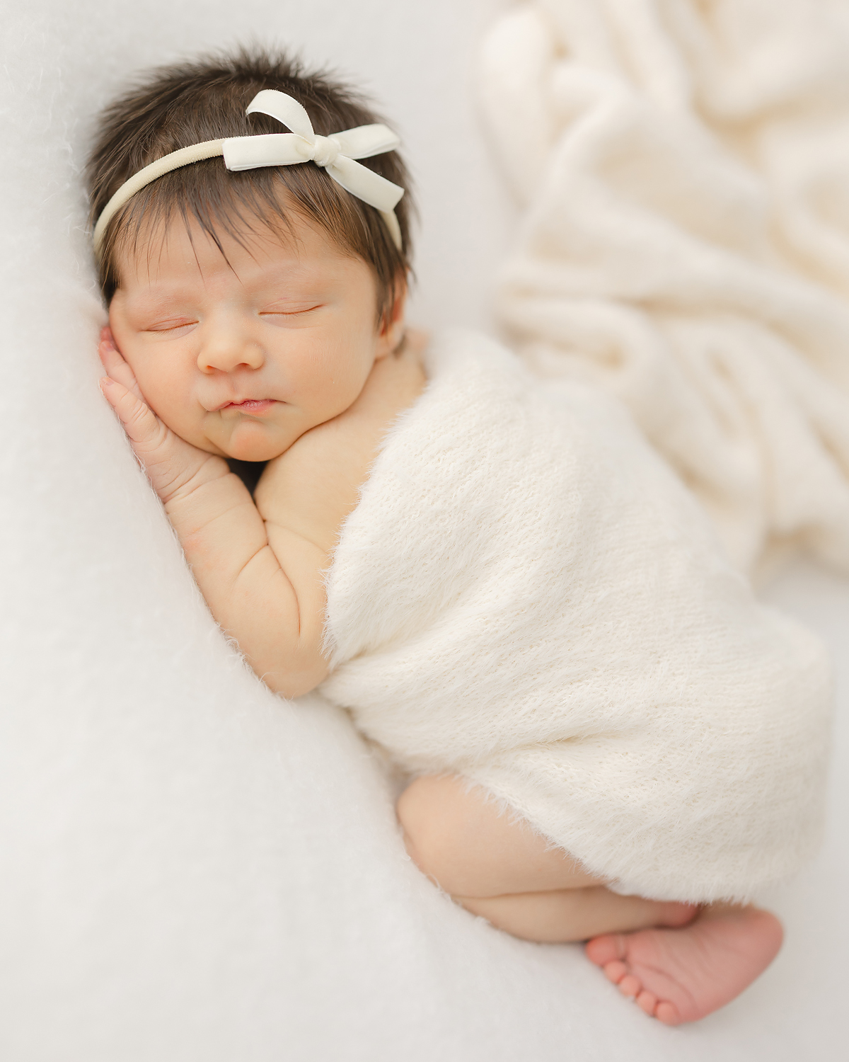 Newborn baby girl snuggled sleepily under a cozy cream wrap during her newborn photo session with Christy Johnson Photography in Wake Forest, NC
