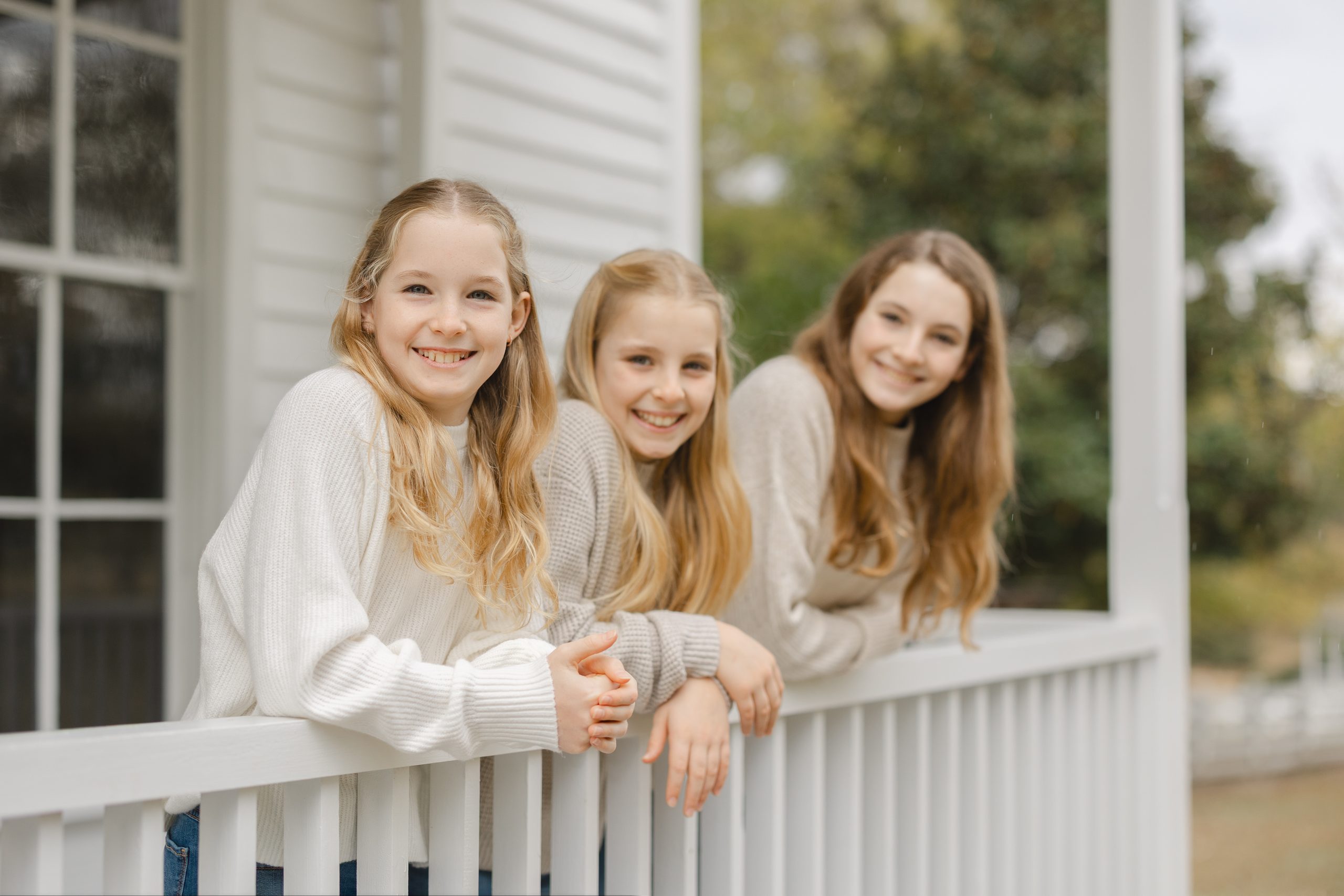 Three sisters in sweaters and jeans smile during their family photos in Raleigh NC